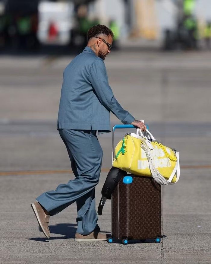 Neymar thu hút sự chú ý với phong cách rực rỡ quen thuộc, kết hợp túi du lịch Louis Vuitton Keepall Bandoulìere màu vàng trị giá hơn 10.000 USD. Ngôi sao Brazil tạo điểm nhấn với vali LV Horizon 55 phối chi tiết màu xanh dương. Sự kết hợp giữa hai gam màu vàng - xanh gợi liên tưởng đến màu sắc quốc kỳ Brazil.