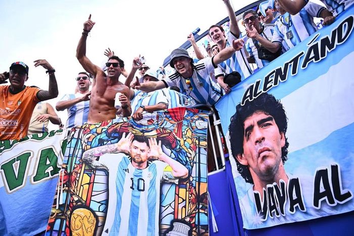 Các cổ động viên Argentina mang theo những lá cờ khổ lớn in hình Messi và cố huyền thoại Diego Maradona. Những biểu ngữ này được giăng kín khán đài, như sự kết nối giữa hai thế hệ biểu tượng vĩ đại nhất lịch sử bóng đá Argentina. Trong ngày Messi lập hat-trick và cân bằng kỷ lục ghi bàn tại World Cup, khán đài Kansas thực sự trở thành một lễ hội tôn vinh huyền thoại sống của bóng đá thế giới.