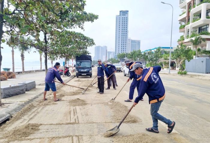 Nhân viên Công ty Cổ phần Cầu đường Đà Nẵng xúc dọn cát tràn trên mặt đường Võ Nguyên Giáp. Ảnh: NGỌC BÍCH