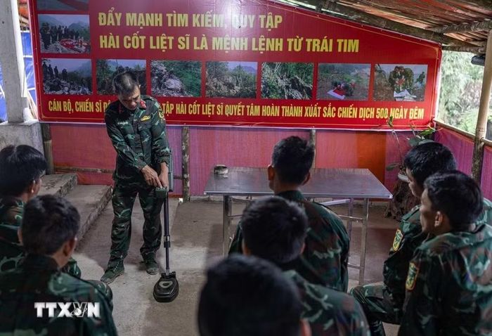 Thiếu tá quân nhân chuyên nghiệp Lê Văn Quyết hướng dẫn các thành viên trong Đội sử dụng máy dò mìn, đảm bảo an toàn khi tìm kiếm. (Ảnh: Hoàng Hiếu/TTXVN)
