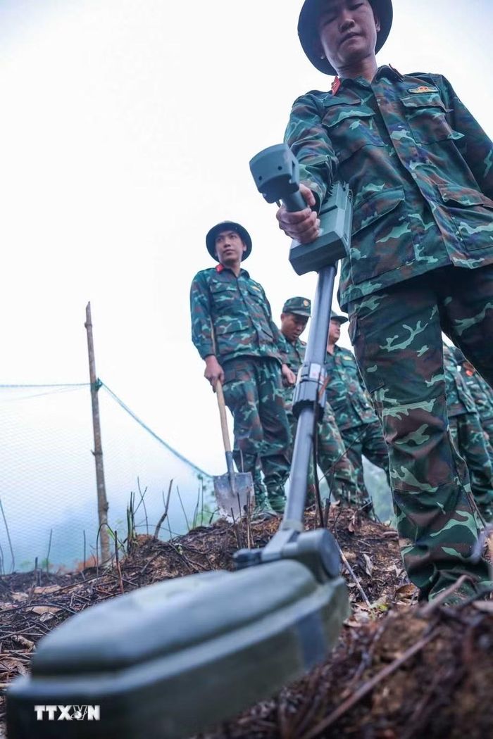 Các thành viên Đội tìm kiếm, quy tập hài cốt liệt sỹ sử dụng máy dò mìn để đảm bảo khu vực tìm kiếm "sạch" trước khi tiến hành tìm kiếm. (Ảnh: Hoàng Hiếu/TTXVN)