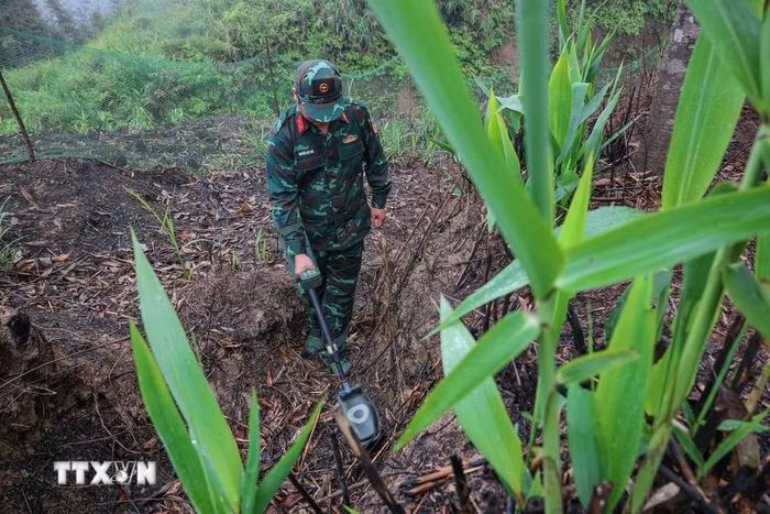 Các thành viên Đội tìm kiếm, quy tập hài cốt liệt sỹ sử dụng máy dò để tìm kiếm, xử lý bom mìn, vật liệu nổ còn sót lại tại khu vực tìm kiếm, quy tập hài cốt liệt sỹ. (Ảnh: Hoàng Hiếu/TTXVN)