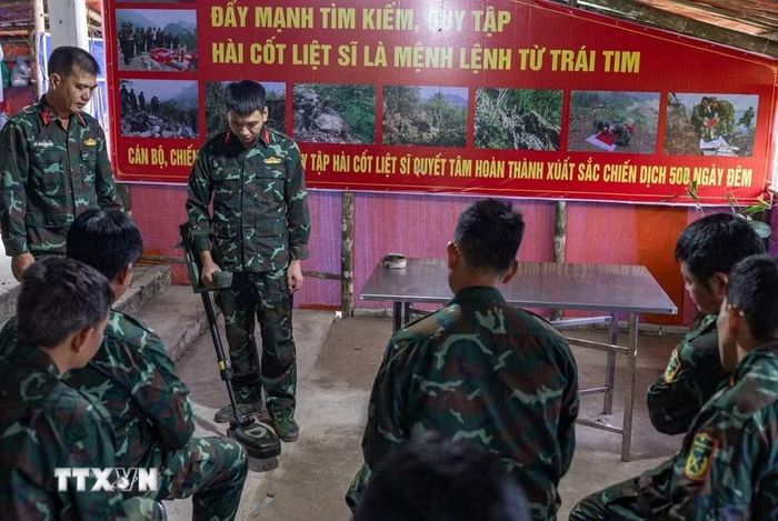 Thiếu tá quân nhân chuyên nghiệp Lê Văn Quyết hướng dẫn các thành viên trong Đội sử dụng máy dò mìn, đảm bảo an toàn khi tìm kiếm. (Ảnh: Hoàng Hiếu/TTXVN)