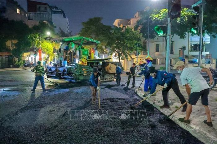 Công nhân cùng máy móc được huy động làm việc liên tục để thảm nhựa mặt đường trên tuyến phố Quang Trung.