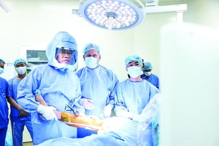 PGS.TS. Đào Xuân Thành (đội mũ trùm) và kíp mổ của Bệnh viện Đại học Y Hà Nội đang sử dụng robot CORI trong quá trình phẫu thuật thay khớp gối cho bệnh nhân. Ảnh: BVCC.