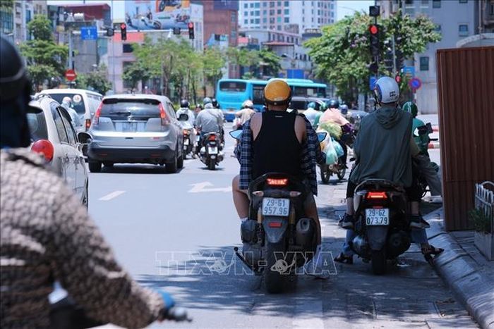 Người tham gia giao thông trên đường Tây Sơn dừng xe dưới râm tránh ánh nắng gay gắt trong lúc chờ đèn tín hiệu giao thông.