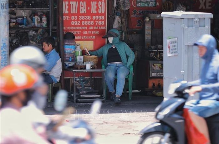 Dù ngồi trong bóng râm, người dân ven đường Võ Thị Sáu vẫn phải mặc đồ chống nắng do thời tiết oi bức.