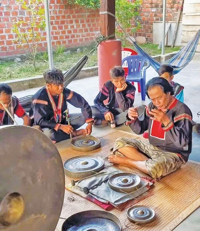  Nghệ nhân Ưu tú Nay Phai (bìa phải) dạy cách phân biệt thang âm của mỗi loại cồng chiêng cho thế hệ trẻ. Ảnh: Ngô Mạo 