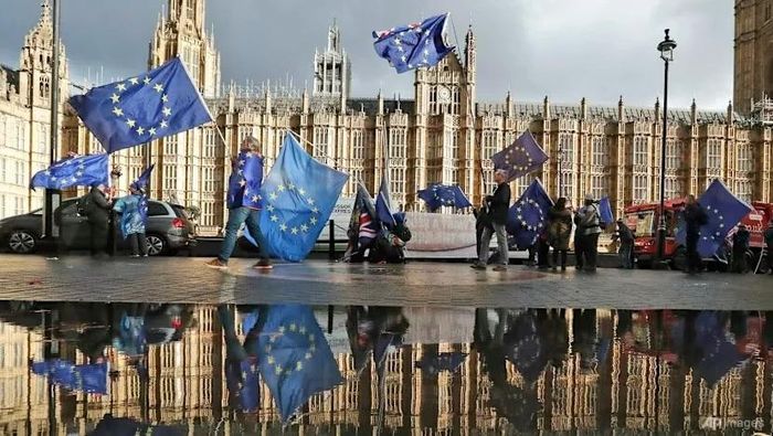 Hình ảnh người biểu tình phản đối Brexit được phản chiếu trong một vũng nước lớn khi họ vẫy cờ châu Âu trước tòa nhà Quốc hội ở London, ngày 3 tháng 12 năm 2018. Ảnh: AP