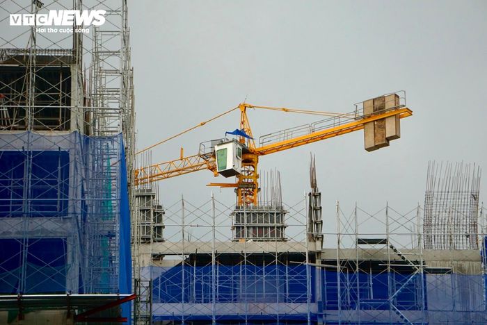 Trên công trường, cần cẩu tháp hoạt động liên tục, phục vụ việc vận chuyển vật tư, thiết bị. Hệ thống lưới bảo hộ phủ kín các mặt công trình để đảm bảo an toàn trong quá trình xây dựng.