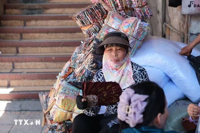 Khăn che mặt, mũ rộng vành và quạt tay trở thành vật dụng quen thuộc của người bán hàng khi phải ngồi nhiều giờ ngoài trời. (Ảnh: Phạm Tuấn Anh/TTXVN)