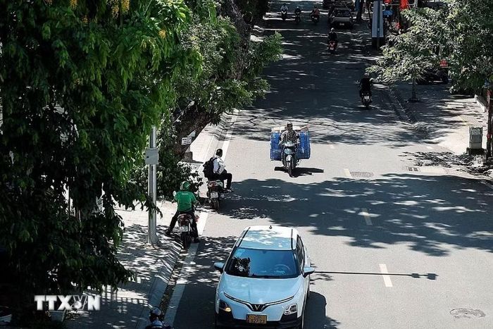 Dòng phương tiện thưa hơn vào giữa trưa; nhiều người đi xe máy cố bám sát các khoảng bóng cây để giảm bớt hơi nóng từ mặt đường. (Ảnh: Phạm Tuấn Anh/TTXVN)