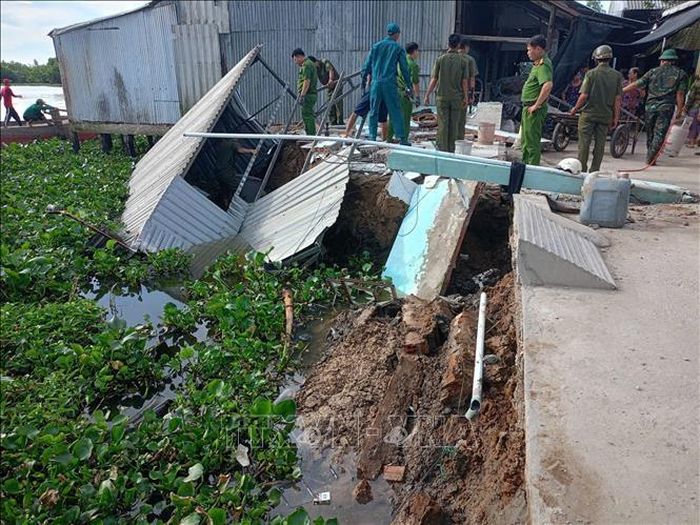 Lực lượng chức năng khoanh vùng khu vực nguy hiểm, hỗ trợ các hộ dân di dời tài sản và động viên hộ dân bị sạt lở nhà. Ảnh: TTXVN phát