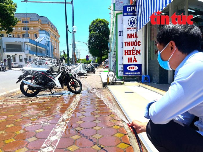 Người dân dùng vòi nước để tưới mát cho chiếc xe máy trước khi di chuyển.
