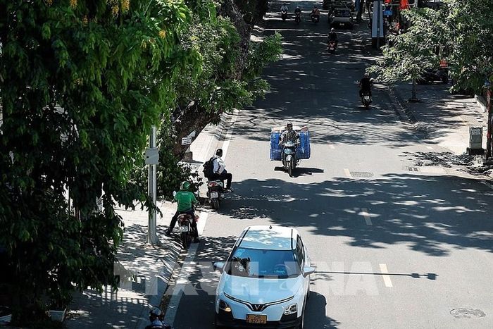 Dòng phương tiện thưa hơn vào giữa trưa; nhiều người đi xe máy cố bám sát các khoảng bóng cây để giảm bớt hơi nóng từ mặt đường. Ảnh: Phạm Tuấn Anh - TTXVN
