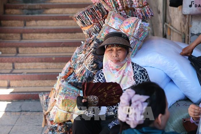 Khăn che mặt, mũ rộng vành và quạt tay trở thành vật dụng quen thuộc của người bán hàng khi phải ngồi nhiều giờ ngoài trời. Ảnh: Phạm Tuấn Anh - TTXVN