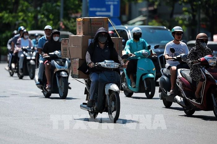 Người giao hàng bằng xe máy phải phủ kín người bằng áo chống nắng, khẩu trang và mũ để thích nghi với thời tiết khắc nghiệt. Ảnh: Phạm Tuấn Anh - TTXVN