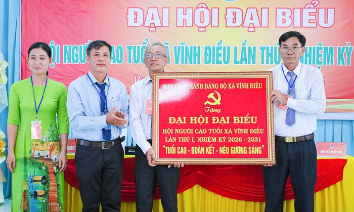 Phó Bí thư Thường trực Đảng ủy xã Vĩnh Điều Huỳnh Thiện Khoa (thứ hai, từ trái qua) trao bức trướng cho Đại hội.