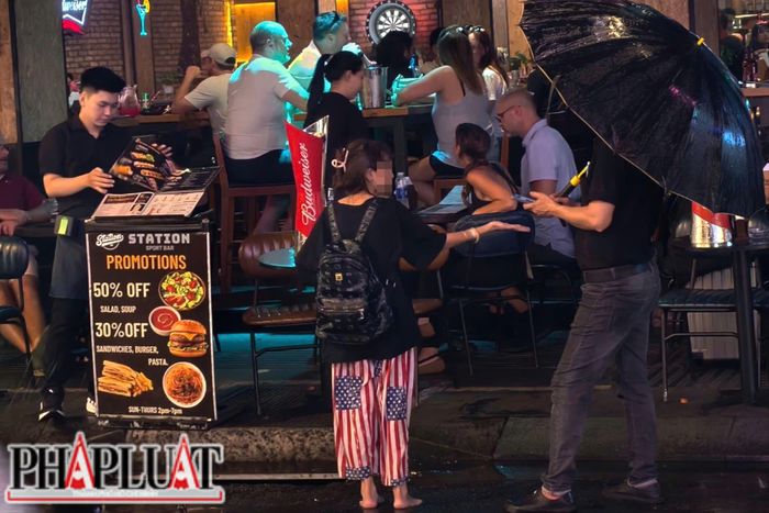  Dưới cơn mưa lất phất đầu mùa, một bé gái ôm em nhỏ đứng trước quán ăn đông khách, chờ đợi sự giúp đỡ từ những người xa lạ qua lại trên tuyến phố. Ảnh: NHÓM PV 