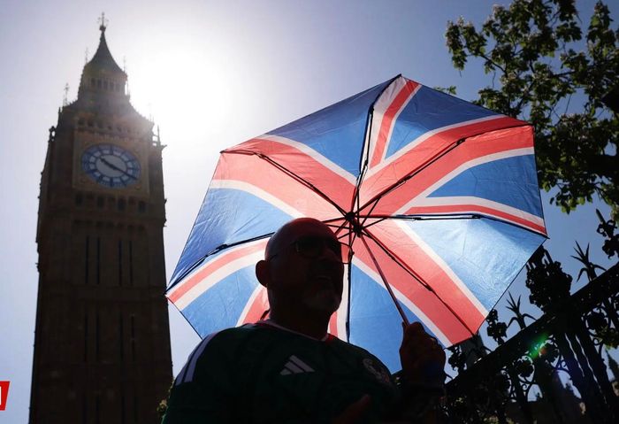 Một người đi bộ giương ô tránh nắng khi đi ngang qua tòa nhà Quốc hội ở London, Anh. Ảnh: EPA