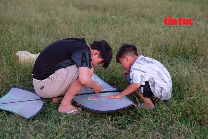 Các em nhỏ cùng nhau hỗ trợ chỉnh sửa diều, tạo nên những kỷ niệm đẹp trong mùa hè.