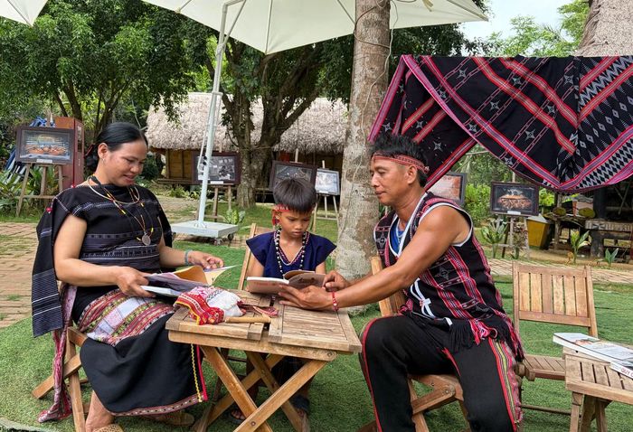 Một gia đình đồng bào các dân tộc Tây Nguyên ở Làng Văn hóa - Du lịch các dân tộc Việt Nam chọn sách để "kết nối" với con. (Ảnh: CTV/Vietnam+)