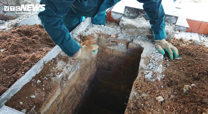 Cán bộ dân quân cúi mình, cẩn thận bốc từng lớp đất sau khi đào đến phần có tiểu quách. (Ảnh: Tiến Thắng)