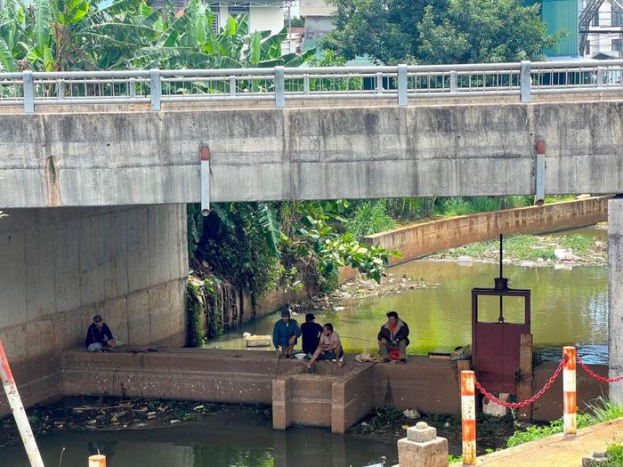 Một số người dân câu cá dưới cầu trên, bao quanh bởi rác.