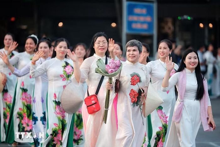 Những tà áo dài trắng thêu họa tiết sen cùng hoa sen cầm tay tạo nên hình ảnh thanh lịch, gần gũi trong đoàn diễu hành bên Hồ Tây, góp phần tôn vinh vẻ đẹp áo dài Việt Nam và biểu tượng hoa sen. (Ảnh: Phạm Tuấn Anh/TTXVN)