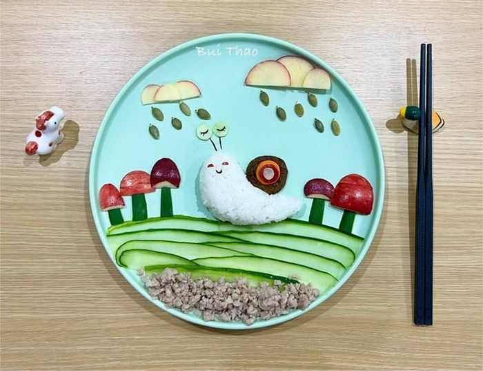 Ốc sên mang cái vỏ trên lưng làm từ nấm hương khô, các hạt mưa làm từ hạt bí xanh. Chị chọn những miếng táo có màu khác nhau để bức tranh cơm của mình sống động hơn. ẢNH: NVCC
