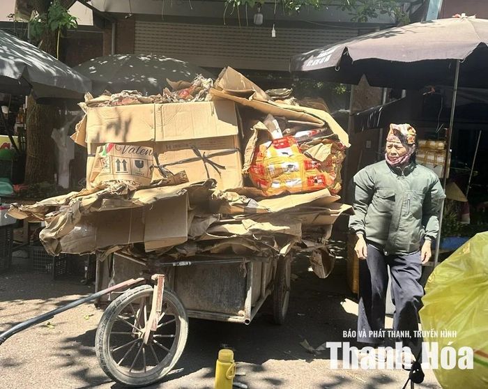 Bà Nguyễn Thị Hải thu gom phế liệu dưới nắng nóng tại Chợ đầu mối rau quả, thực phẩm Đông Hương, phường Hạc Thành.