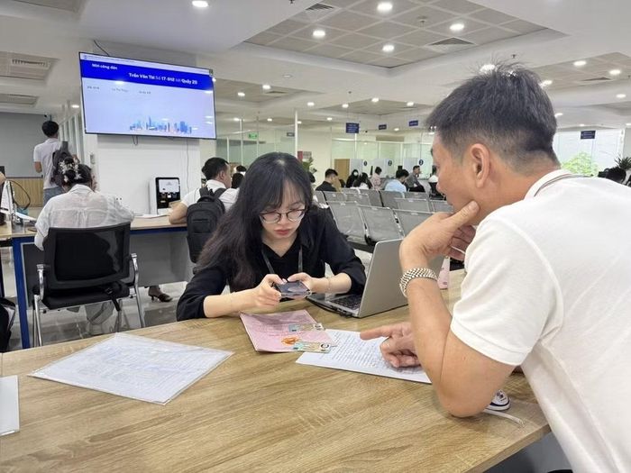 Cán bộ Trung tâm phục vụ hành chính công hướng dẫn người dân lấy số thứ tự online đối với hồ sơ liên quan đến đất đai qua ứng dụng iHanoi. (Ảnh: Quốc Lũy/TTXVN)
