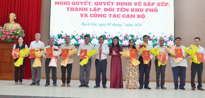 Ủy viên Ban Thường vụ Tỉnh ủy, Bí thư Đảng ủy phường Rạch Giá Mai Hoàng Khởi (thứ sáu, từ trái qua); Phó Chủ tịch UBND phường Rạch Giá Nguyễn Thị Hồng Linh (thứ sáu, từ phải qua) trao quyết định cho đại diện các khu phố.