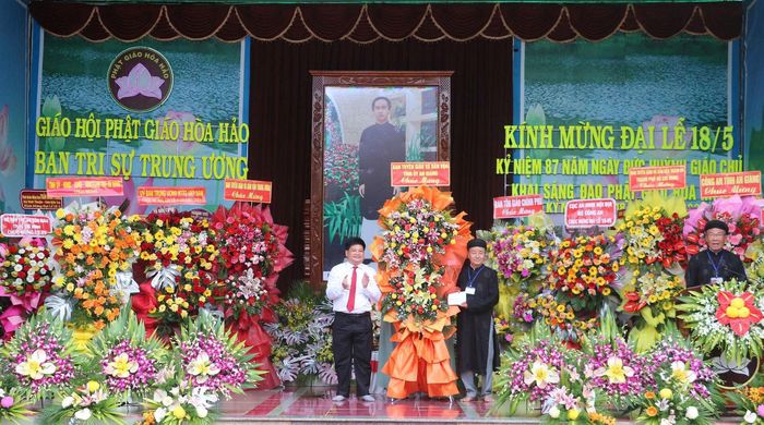 Ông Tống Phước Trường, Trưởng ban Tuyên giáo và Dân vận Tỉnh ủy An Giang (trái) tặng hoa, chúc mừng Đại lễ kỷ niệm 87 năm Ngày khai sáng đạo Phật giáo Hòa Hảo