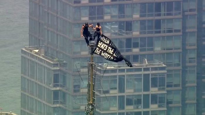 Hai người đứng trên đỉnh cột ăng-ten của tòa nhà Empire State ở New York và giơ cao một biểu ngữ, ngày 1/7. Ảnh: Getty.