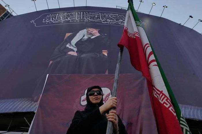 Một phụ nữ ủng hộ chính phủ cầm cờ Iran dưới một biểu ngữ có hình chân dung của cố Lãnh tụ tối cao, Đại giáo chủ Ali Khamenei, tại quảng trường trung tâm thủ đô Tehran của Iran, ngày 30/6/2026. Ảnh: AP.