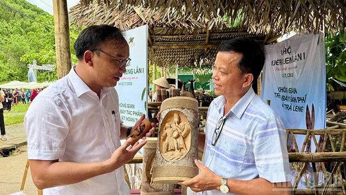 Chủ tịch Ủy ban nhân dân xã Trà Leng Châu Minh Nghĩa (áo trắng) trao đổi với nghệ nhân điêu khắc trên thân vỏ cây quế.