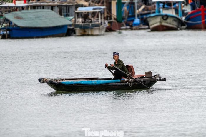 Vào lúc ngớt mưa, người phụ nữ tất bật chèo đò để đưa ngư dân ra thăm thuyền.