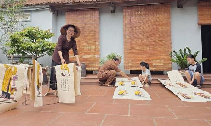 Vợ chồng Nghệ nhân Ưu tú Nguyễn Thị Oanh cùng các cháu nội phơi tranh.