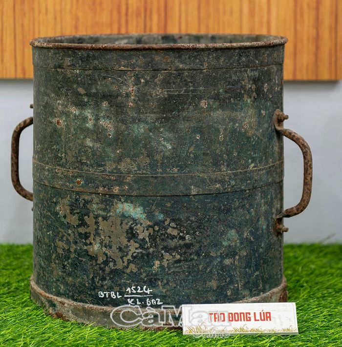 Chiếc thùng sắt đúc có quai cầm (táo đong lúa) lưu dấu vết thời gian, là dụng cụ đo lường lúa gạo thô sơ.