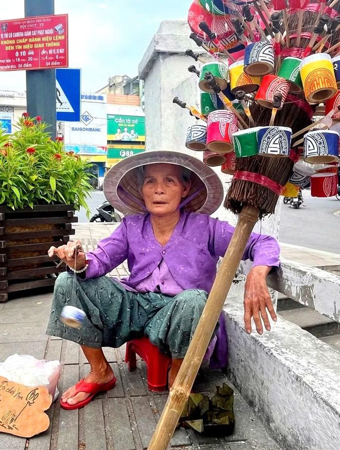 Mệ Hường cầm trò chơi con ve ve xoay vòng phát ra tiếng vui tai, mời chào khách vào mua ủng hộ.