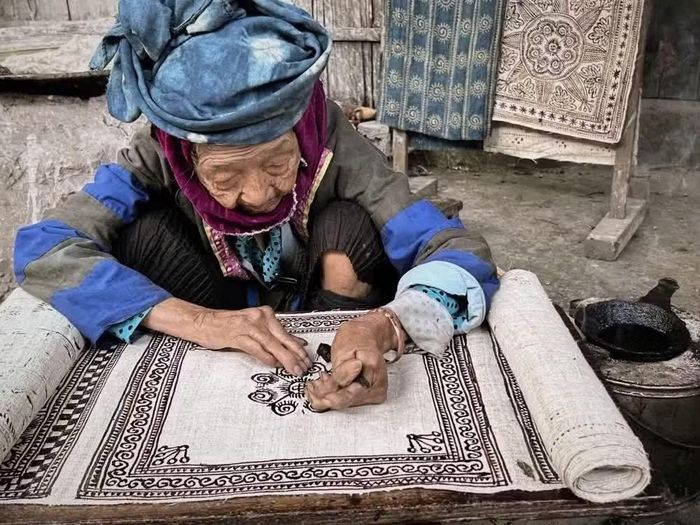 Nghệ nhân cao tuổi vẽ hoa văn bằng sáp ong trên nền vải lanh. (Ảnh: Phương Anh/TTXVN phát)