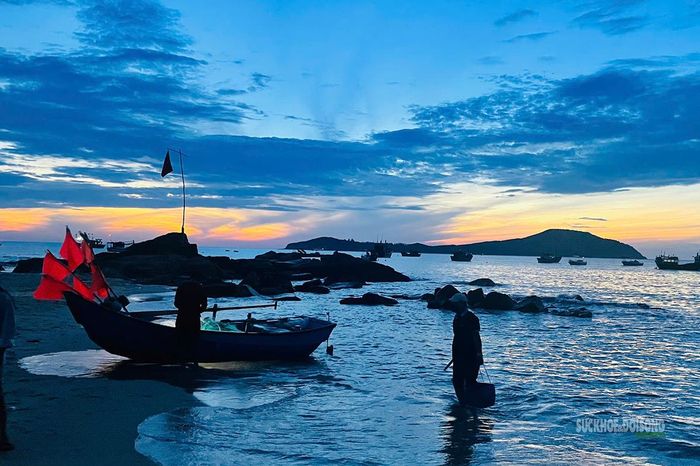 Một ngư dân xách túi hải sản từ mép nước lên bãi khi trời vừa sáng.