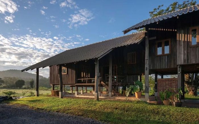 Về mặt kiến trúc, Raintree Lane Farm House sử dụng hình thái mái dốc truyền thống, kết hợp kết cấu gỗ mộc mạc và vật liệu địa phương. Các chi tiết được tiết giảm tối đa. Không có những đường nét cầu kỳ hay mặt đứng phức tạp, toàn bộ công trình hướng đến cảm giác nhẹ nhàng, gần gũi và phù hợp với khí hậu nhiệt đới của Chiang Mai. Nhìn từ xa, ngôi nhà giống như một phần của những ngôi nhà nông thôn truyền thống hơn là một công trình hiện đại.