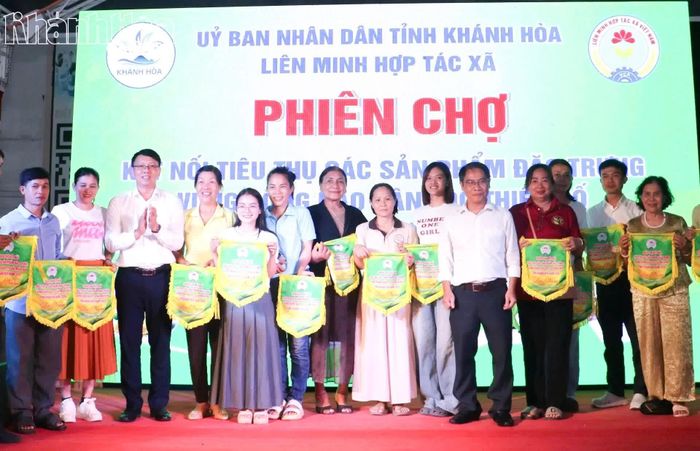 Đồng chí Nguyễn Thanh Hà (thứ 3 từ trái qua) trao cờ lưu niệm cho các đơn vị tham gia phiên chợ.