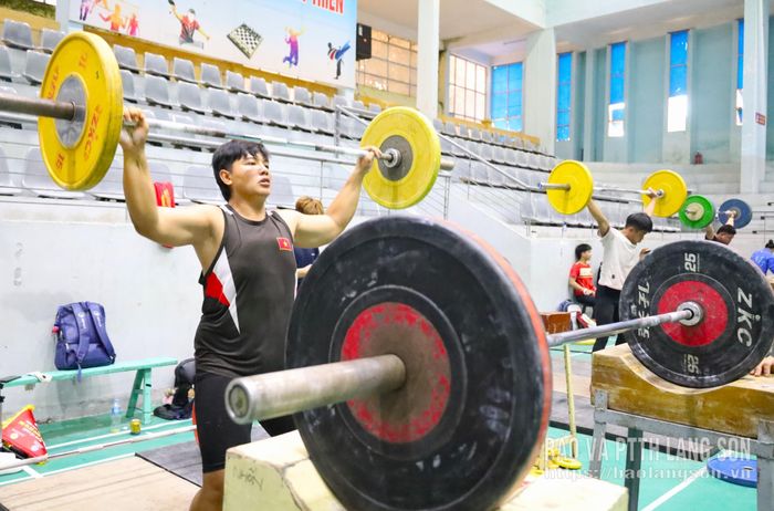 Ngay phía sau sàn thi đấu là khu vực khởi động - nơi các vận động viên tranh thủ hoàn thiện những động tác cuối cùng trước khi bước vào phần thi chính thức. Tại đây, các vận động viên liên tục làm nóng cơ thể, thử mức tạ và điều chỉnh kỹ thuật dưới sự hướng dẫn của huấn luyện viên trước khi được gọi tên lên sàn thi đấu. Những phút chuẩn bị ấy không chỉ quyết định trạng thái thể lực mà còn góp phần tạo nên sự tự tin để mỗi đô cử bước ra sàn đấu với phong độ tốt nhất.