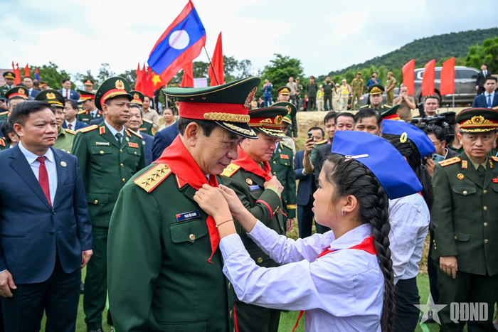 Học sinh Trường Tiểu học Thongnamoun ở huyện Xaychamphone, tỉnh Bolykhamxay (Lào) đeo khăn quàng đỏ cho Đại tướng Phan Văn Giang và Đại tướng Khamliang Outhakaysone. 