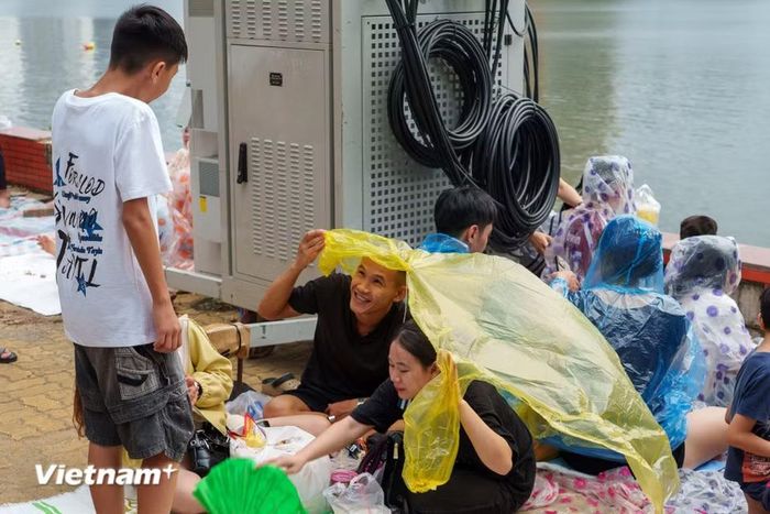 Những chiếc áo mưa, ô dù được tận dụng tối đa để che chắn trong lúc mỏi mòn chờ đợi pháo hoa rực sáng. (Ảnh: Thanh Phong/Vietnam+)