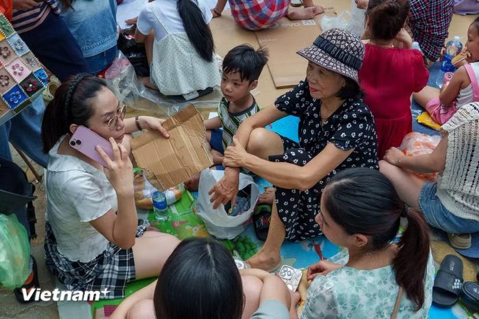 Những tấm bìa carton được tận dụng lót chỗ ngồi và trở thành cái quạt tạm để xua tan không khí oi nóng. (Ảnh: Thanh Phong/Vietnam+)
