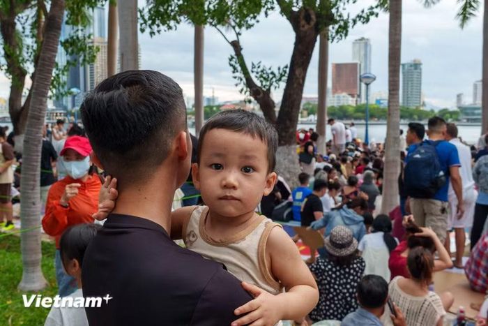 Một em nhỏ được người thân bế trên tay, ngơ ngác giữa biển người đông đúc chờ xem pháo hoa. (Ảnh: Thanh Phong/Vietnam+)